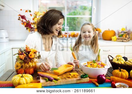 Mother And Daughter Cutting Pumpkin, Onion And Carrot, Cooking Soup For Autumn Meal. Mom And Child C