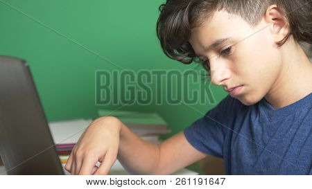 Profile Of A Teenager Boy, On A Green Background. Close-up. The Boy Is Concentrating On The Laptop S