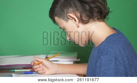 Profile Of A Teenager Boy, On A Green Background. Close-up. The Boy Is Concentrating On The Laptop S