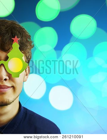Portrait Of A Man In Christmas Glasses. Portrait Of Cheerful, Attractive Man On Blue Sparkles Backgr
