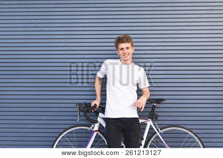 Portrait Of A Happy Guy In A White T-shirt Standing With A White Bike Against The Wall, Looking At T