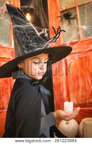 Caucasian Boy In Farytale Carnival Wizard Costume Holding Candle In Hand On Haloween Decor Backgroun