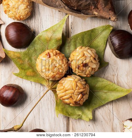 high angle view of some chestnuts and some panellets, as a typical snack eaten in All Saints Day in Catalonia, Spain, called castanada, and some autumn leaves on a wooden table