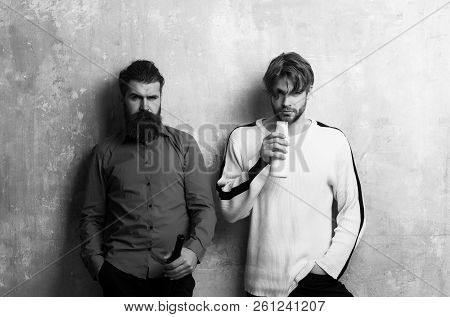Two Serious Friends In Casual Wear Standing With Bottles On Beige Wall. Handsome Man With Yogurt Or 