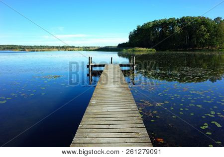 Wooden bridge in lake with calm water and blue sky in Sweden, Scandinavia, Europe. Peaceful outdoor image on Malaren lake in Vastmanland