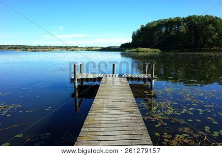 Small wooden bridge in lake with calm water and blue sky in Sweden, Scandinavia, Europe. Peaceful outdoor image on Malaren lake in Vastmanland