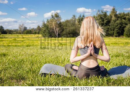 Young Female With Open Arms And Long Blond Hair Sitting Back And Relaxes In Yoga Pose In Green Natur