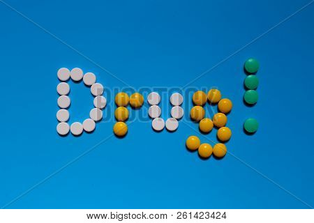 Word Drugs From Color Capsules On The Blue Background. Top View Copy Space Pattern