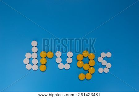 Word Drugs From Color Capsules On The Blue Background. Top View Copy Space Pattern