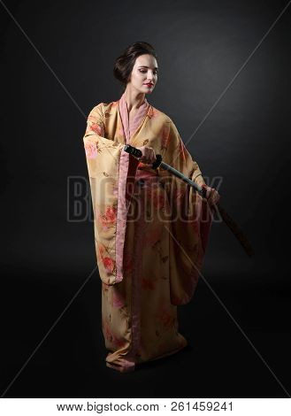 Beautiful Girl In Kimono With Japanese Sword Katana On A Black Background.