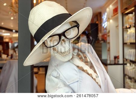 Human Sceleton And Funny Skull In Glasses And Hat Smiling At Door Of Shopping Mall. Original Design 