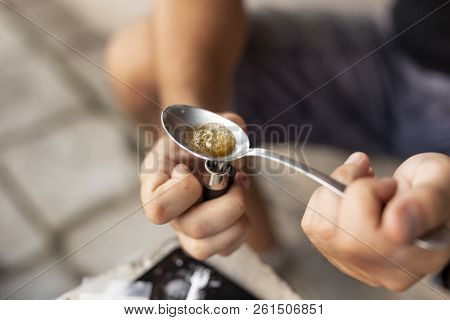 High Angle View Of Male Hands Cooking Heroin In A Spoon With A Lighter, Getting It Ready For Intrave