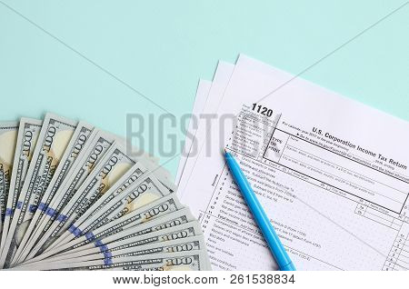 1120 Tax Form Lies Near Hundred Dollar Bills And Blue Pen On A Light Blue Background. Us Corporation