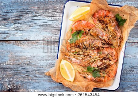 Traditional fried black tiger prawn with lemon as top view in a white casserole on a wooden blue board with copy space left