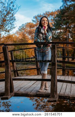 Young Happy Woman Standing On A Wooden Bridge Over The Little Lake In The Park And Enjoying In A Bea