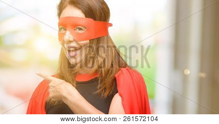 Middle age super hero woman wearing red mask and cape pointing away side with finger