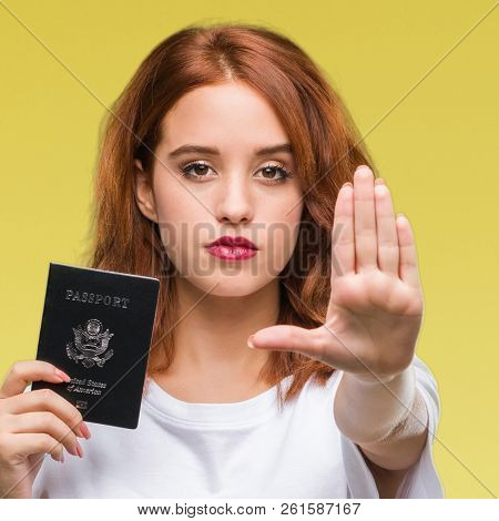 Young beautiful woman holding passport of united states of america over isolated background with open hand doing stop sign with serious and confident expression, defense gesture