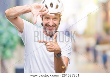 Middle age senior hoary cyclist man wearing bike safety helment isolated background smiling making frame with hands and fingers with happy face. Creativity and photography concept.