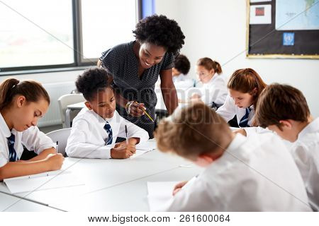 Female High School Tutor Helping Students Wearing Uniform Seated Around Tables In Lesson
