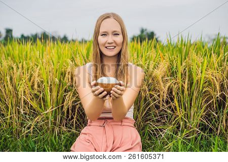 A Woman Is Holding A Cup Of Boiled Rice In A Wooden Cup On The Background Of A Ripe Rice Field