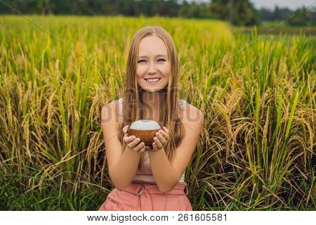 A Woman Is Holding A Cup Of Boiled Rice In A Wooden Cup On The Background Of A Ripe Rice Field