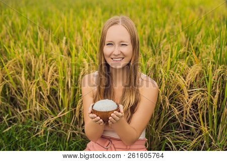 A Woman Is Holding A Cup Of Boiled Rice In A Wooden Cup On The Background Of A Ripe Rice Field