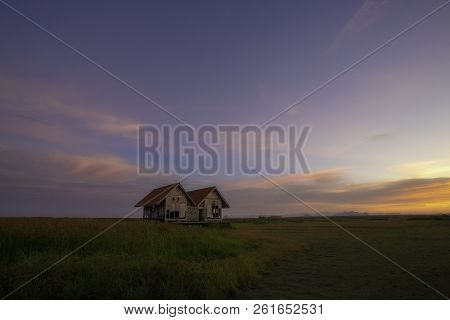 The Old Twin Cottage In The Field At Sunset.