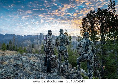 Three Adult Male Hunter Friends, Unrecognizable,  Stand On A Mountain Ridge Looking For Elk To Hunt 