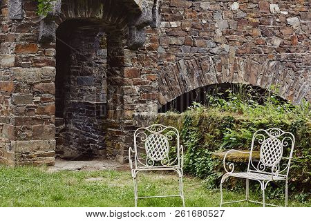 Two Vintage White Chairs Outdoor In Green Courtyard Of Medieval Castle