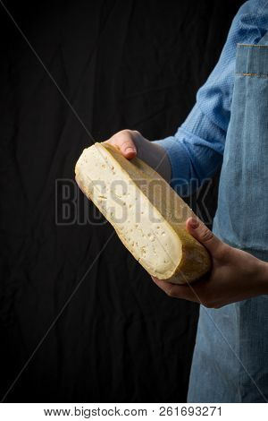 Woman In Blue Apron Holding Taleggio Cheese On Dark Background