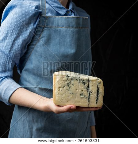 Woman In Apron Holding Piece Of Blue Cheese Gorgonzola On Dark Background