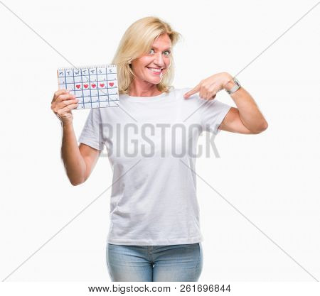 Middle age blonde woman holding menstruation calendar ver isolated background with surprise face pointing finger to himself