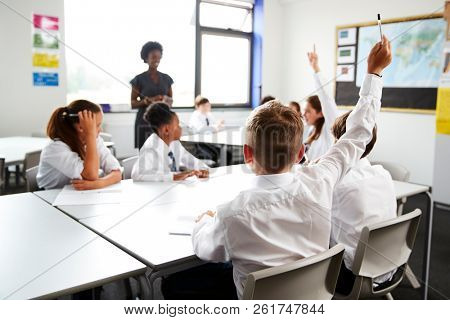 High School Students Wearing Uniform Raising Hands To Answer Question Set By Teacher In Classroom