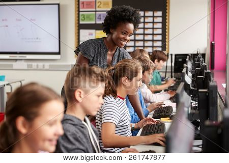 Teacher Helping Female Pupil Line Of High School Students Working at Screens In Computer Class