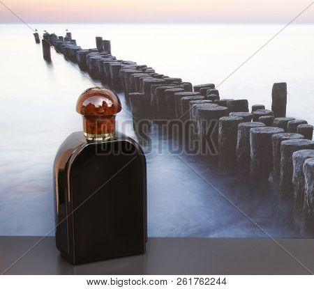 Eau De Toilette, Large Perfume Bottle In Front Of The Picture Of A Groyne In The Sea