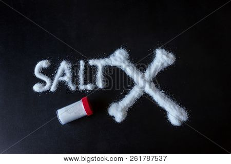 Salt Scattered On Black Surface. Drawn Word- Salt And Crossed Bones. Concept- Healthy Food, Diet, Ha