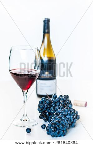 Glass Of Red Wine With A Bottle And A Cluster Of Black Grapes On White Table. Selecive Focus.