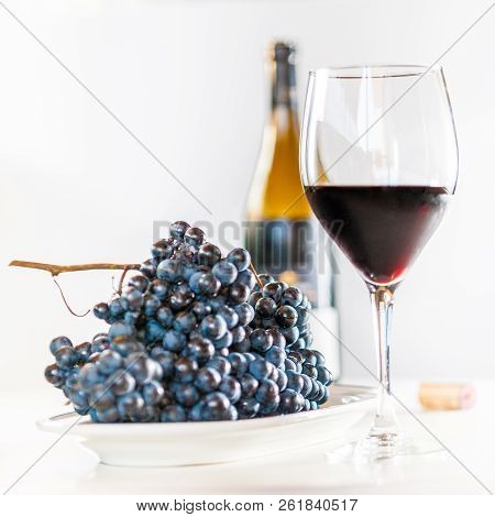Glass Of Red Wine With A Bottle And A Cluster Of Black Grapes On White Table. Selecive Focus.