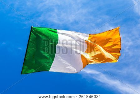 Irish Flag Fluttering In A Brisk Breeze Against A Bright Blue Sky.