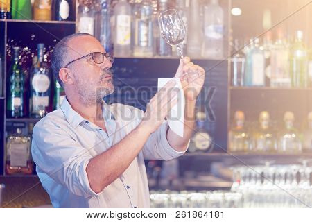 The Bartender Cleans The Glass. A Handsome Bartender Polishes A Glass Of Wine Glasses. The Concept O