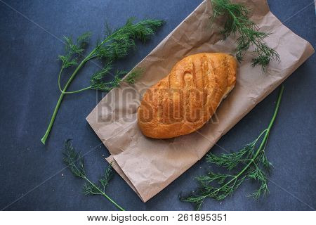 A Loaf Of White Bread On Brown Kraft Paper, Surrounded By Dill On A Dark Background.