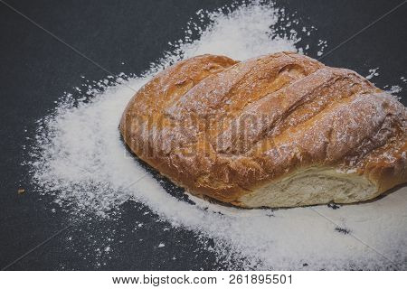 A Loaf Of White Bread On Dark Kraft Paper, Powdered With Flour.
