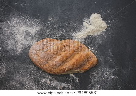 A Loaf Of White Bread On Dark Kraft Paper, Powdered With Flour.