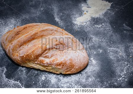 A Loaf Of White Bread On Dark Kraft Paper, Powdered With Flour.