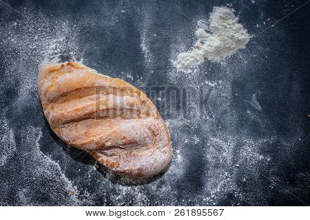 A Loaf Of White Bread On Dark Kraft Paper, Powdered With Flour.