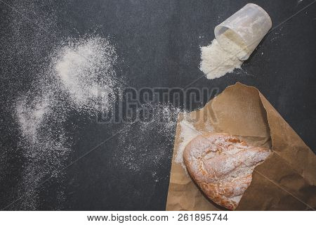 A Loaf Of White Bread On Brown Craft Paper, Powdered With Flour On A Dark Table Background.