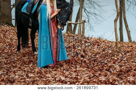 A Girl In A Pink Vintage Dress, With Long Hair, A Blonde In A Blue, Old-fashioned Cape, Stands Besid
