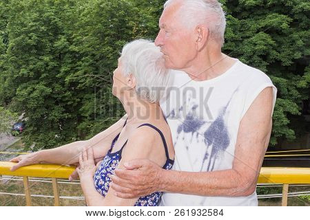 Senior Couple Standing Oustide At Balccony At Home And Looking Awayat Green Trees