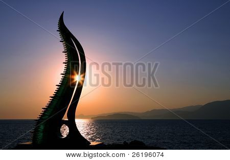Nascer do sol por trás de um monumento municipal em Aghios Nikolaos, Creta