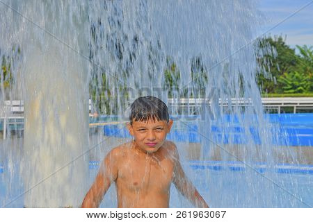 Little Boy In The Small Swimming Pool. Boy Taking Shower In Water Park. Boy Standing Under Sprinkler